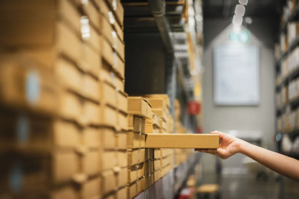 cardboard box package with blur hand of shopper woman picking product from shelf in warehouse 1 min 980x653 1